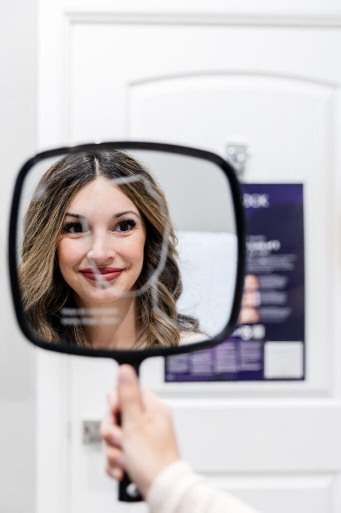 woman smiling while looking into hand mirror after receiving laser scar removal in OKC