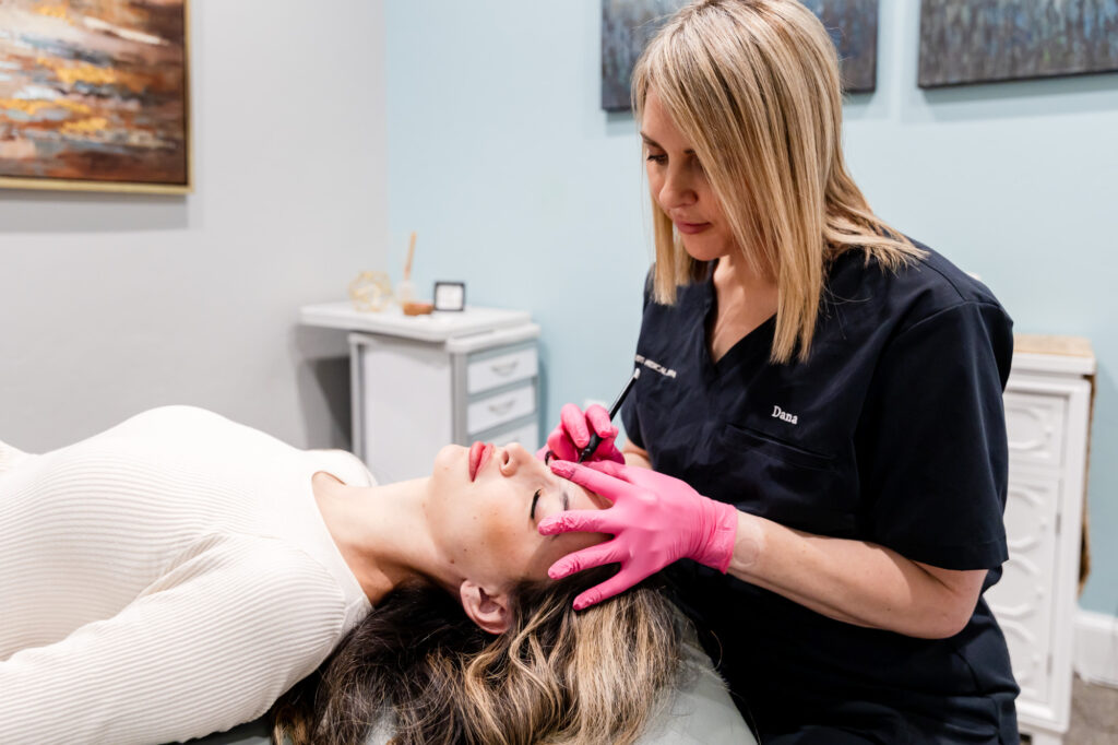 Patient lays down with eyes closed as medical provider places device on her face to improve skin toning in OKC.