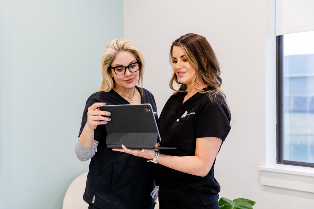 Two women standing together looking at tablet to assess facial contouring in Oklahoma City