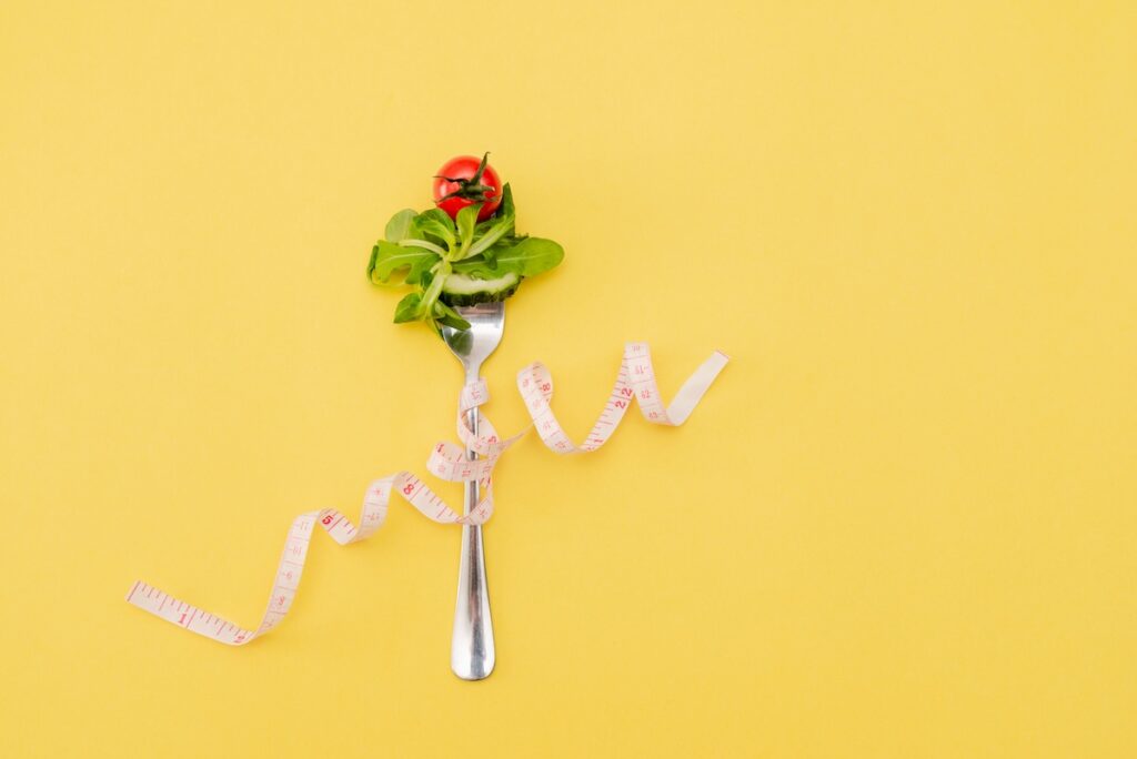 Yellow background with measuring tape wrapped around a fork holding salad to support semaglutide weight loss near Edmond, OK